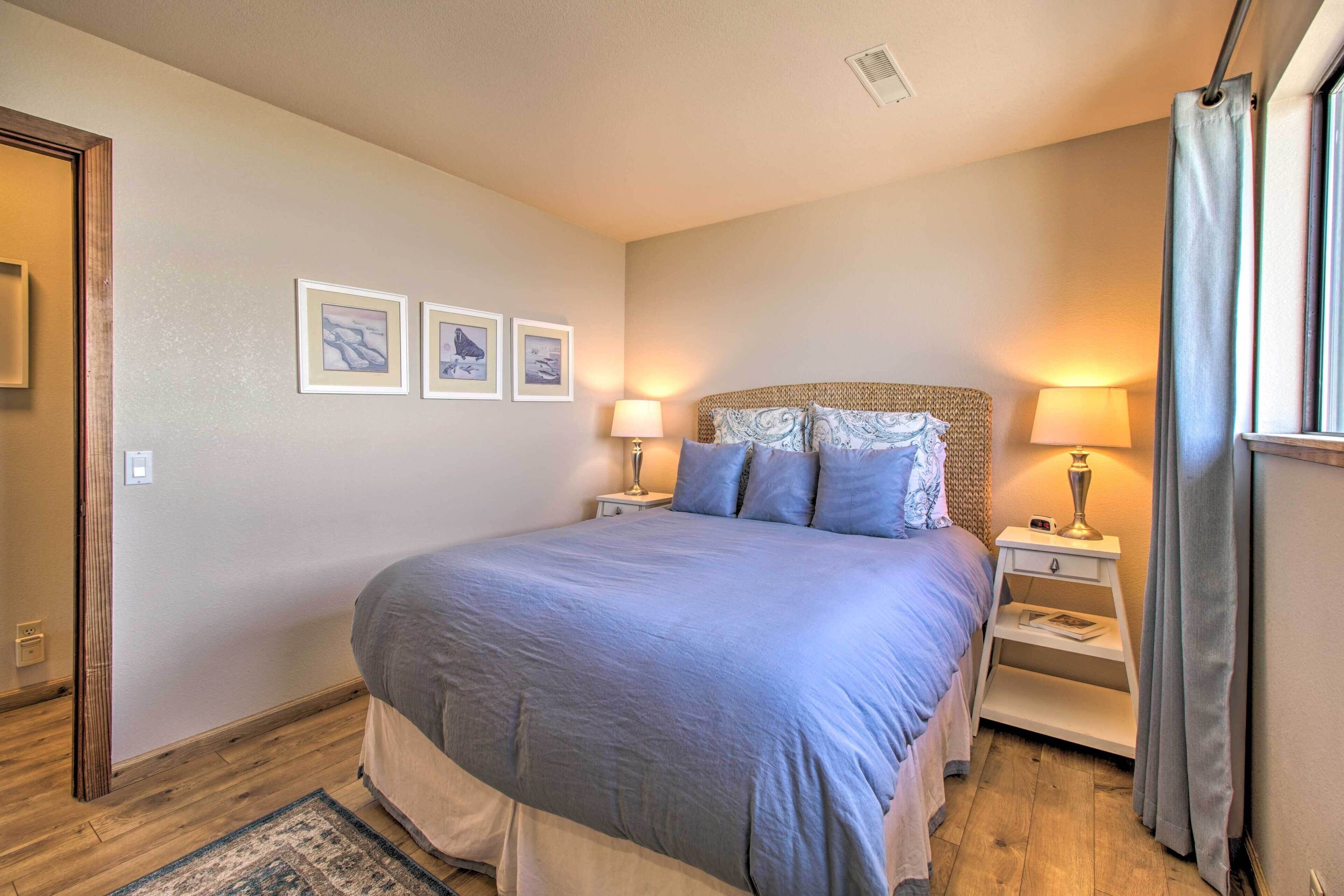 A bedroom with a large bed, two bedside tables with lamps, a nightstand, and a window with curtains.