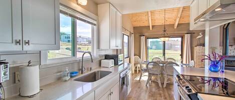 Une cuisine moderne avec des armoires blanches, un grand îlot central, un four encastré et une vue sur l’extérieur.