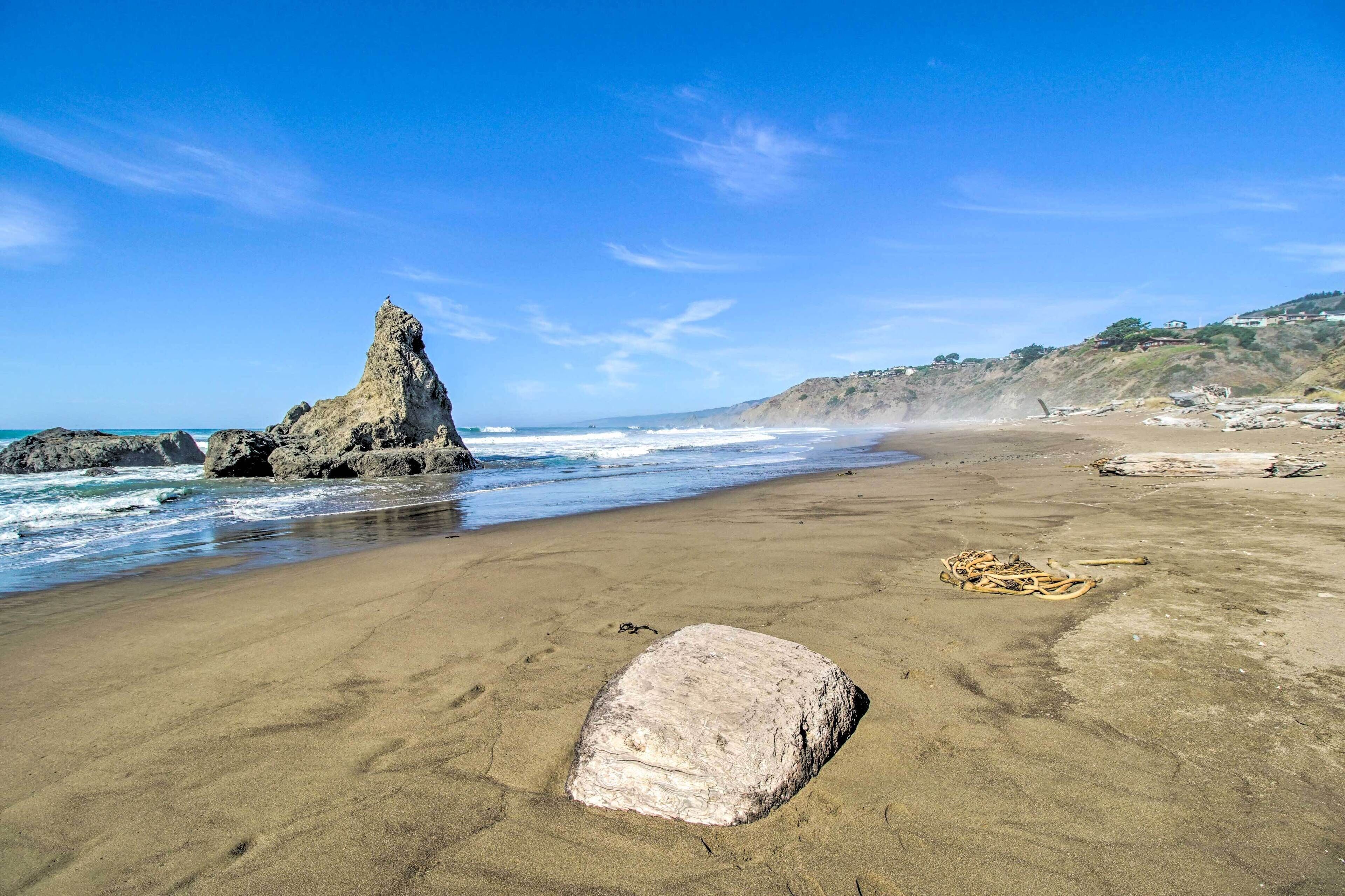 A sandy beach with large rocks and a prominent rock formation.