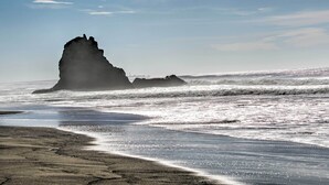 Una playa con una gran formación rocosa a lo lejos y olas acercándose a la orilla.