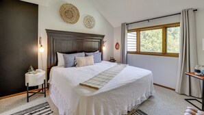 A bedroom with a large bed, a bedside table, a lamp, and a window with curtains.