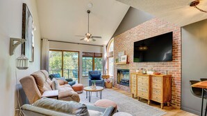 A spacious living room with a fireplace, comfortable seating, and a large TV mounted on a brick wall.
