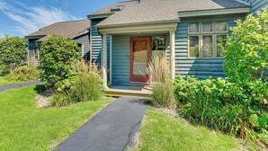 A single-story house with a front porch, a red door, and a small front yard with a pathway leading to the entrance.