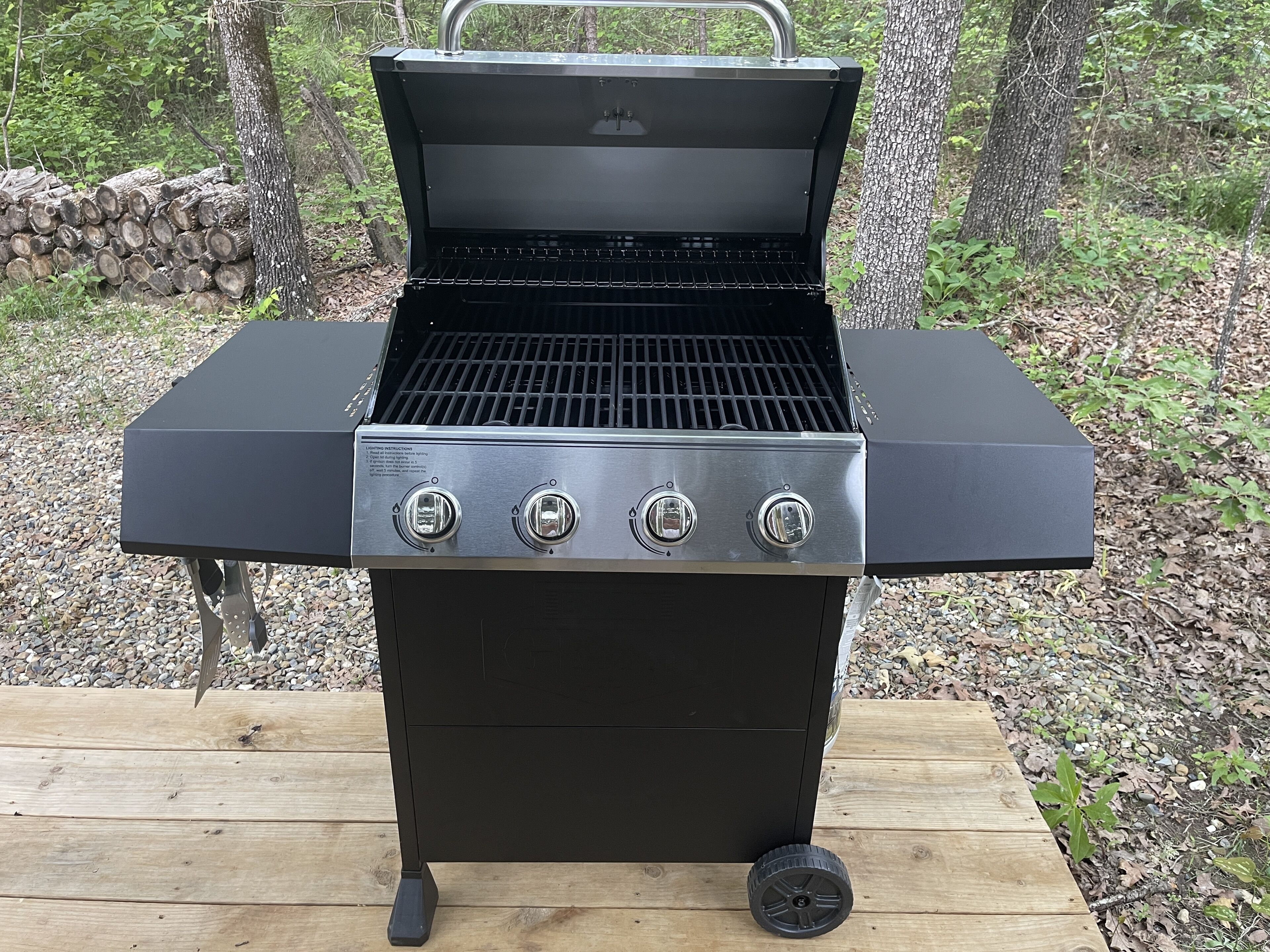 A black outdoor grill with four burners and a wheel for mobility, placed on a wooden deck.