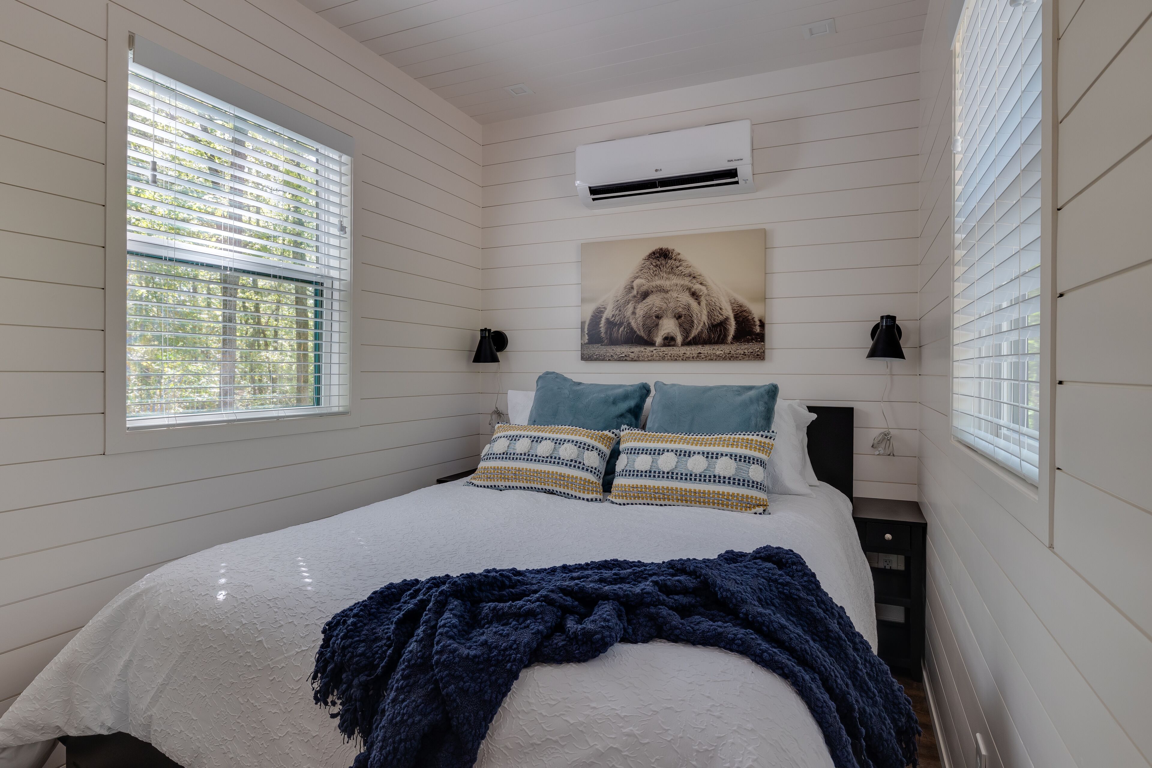A bedroom with a bed, a window with blinds, an air conditioner, and a wall-mounted picture.
