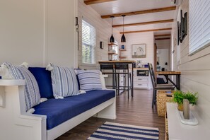 Ein modernes Wohnzimmer mit einem blauen Sofa, Holzbalken, einer Küchenzeile und einem Esstisch.