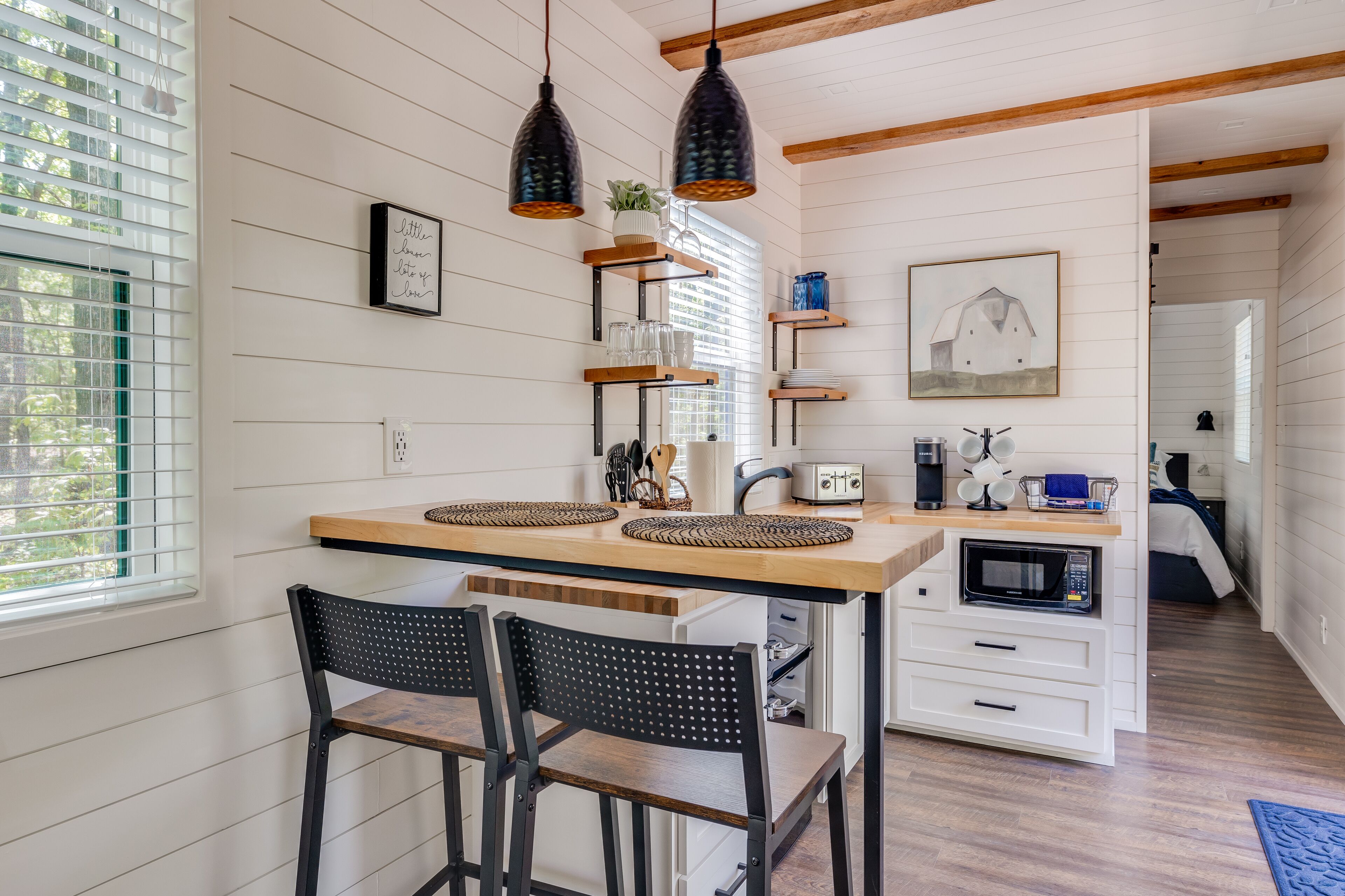 A modern kitchen with wooden countertops, black chairs, and pendant lights.