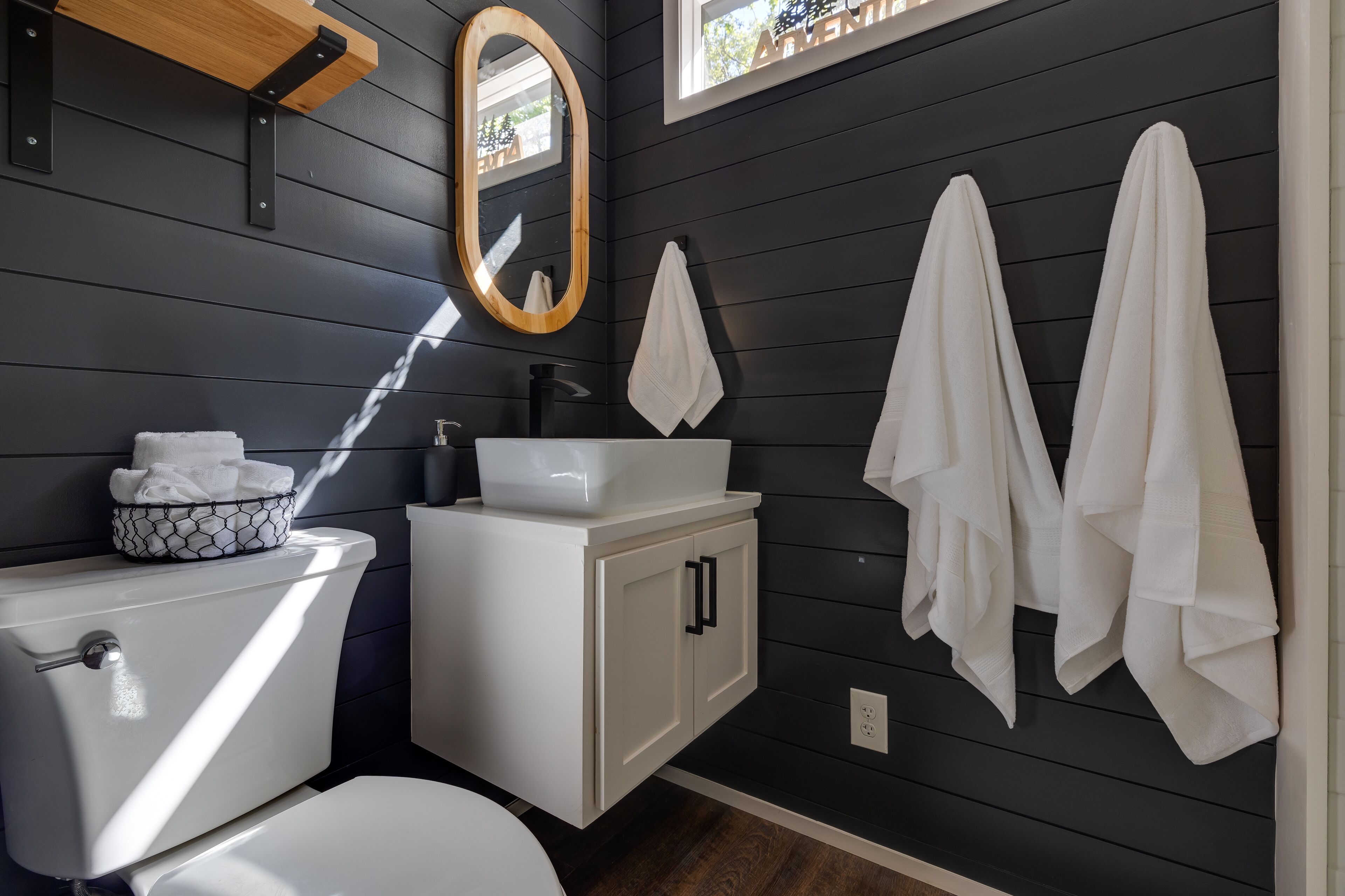 A bathroom with a white toilet, a white sink, and a mirror. There are towels hanging on the wall.