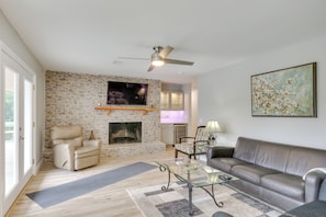 A living room with a stone fireplace, leather sofa, and a flat-screen TV. - Waterfront Lakehouse w/ Private Dock & Fire Pit! (Chapin)