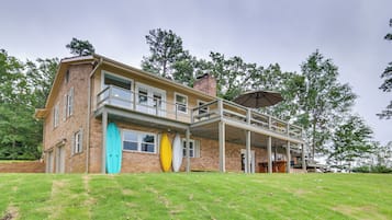 A two-story house with a covered patio, a brick exterior, and a grassy lawn.