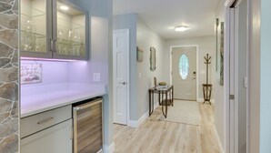 A kitchen with a built-in wine rack, a dining area with a table and chairs, and a hallway leading to a door with a stained glass window. - Waterfront Lakehouse w/ Private Dock & Fire Pit! (Chapin)