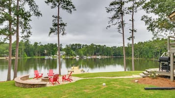 A lakeside patio with red chairs and a fire pit, surrounded by trees and a view of the lake.