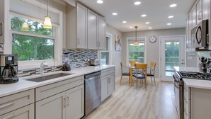 A modern kitchen with a dishwasher, sink, and stove. There is a dining area with chairs and a table. - Waterfront Lakehouse w/ Private Dock & Fire Pit! (Chapin)