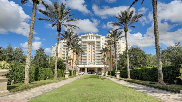 Een groot hotel met een centrale ingang, omringd door palmbomen en een verzorgd gazon.