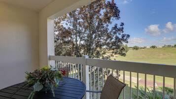 A balcony with a table and chair, overlooking a golf course.