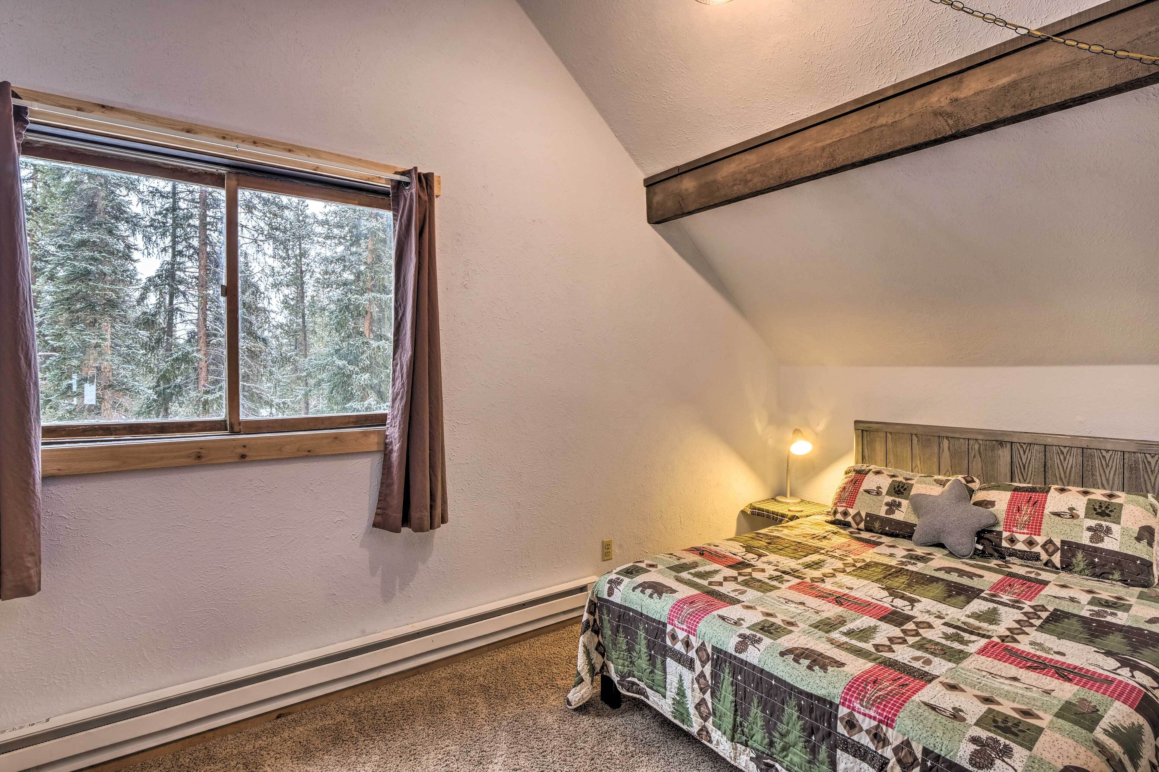 A bedroom with a large window, a bed with a patterned quilt, and a nightstand with a lamp.