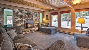 Un salón acogedor con chimenea, una pared de piedra y ventanas amplias con vistas nevadas.