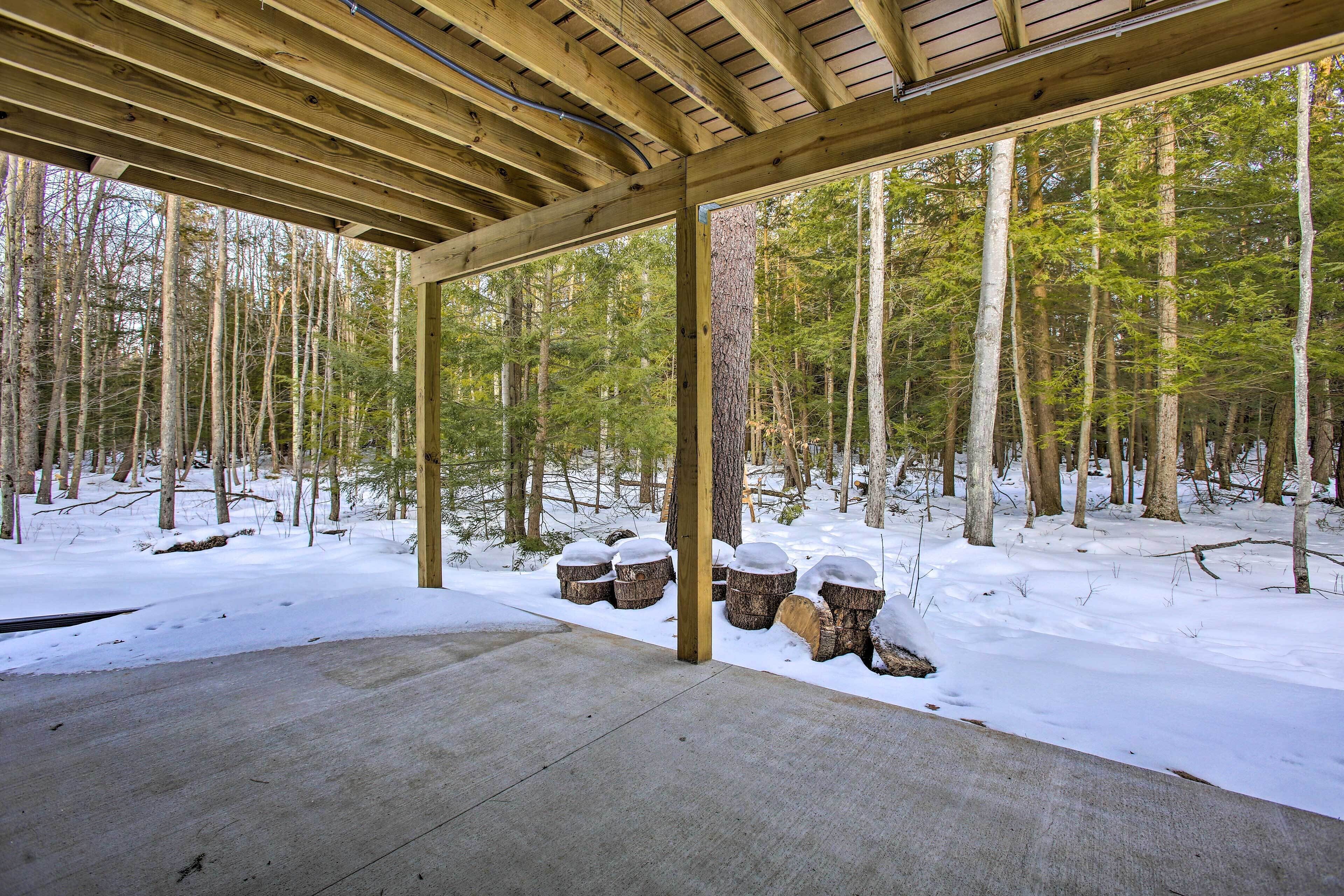 Une structure en bois couverte, dotée d’un plancher en béton, entourée d’un sol enneigé et de grands arbres.