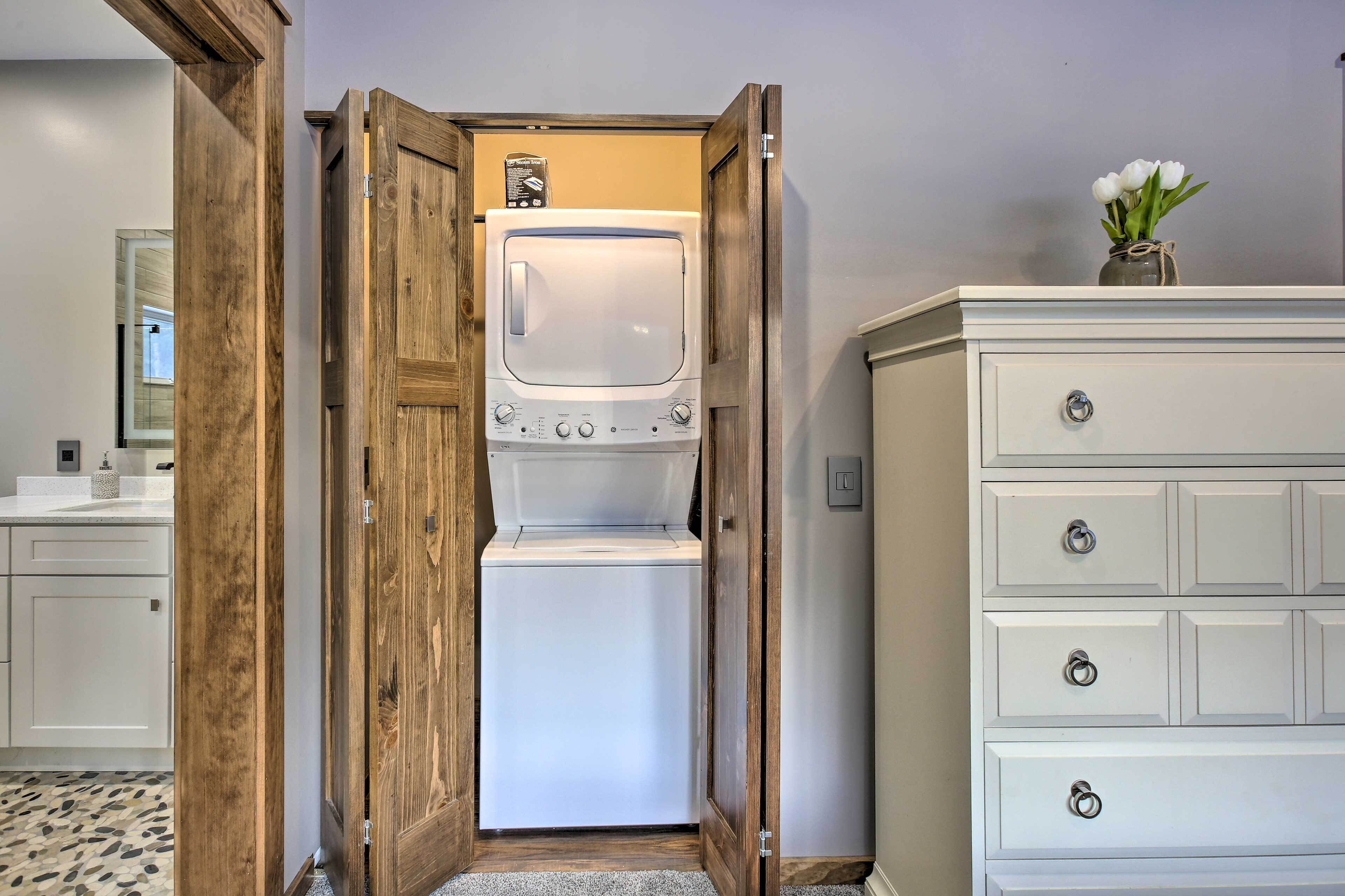 Un lavadero con lavadora y secadora incorporadas, puertas de madera y un aparador blanco con cajones.