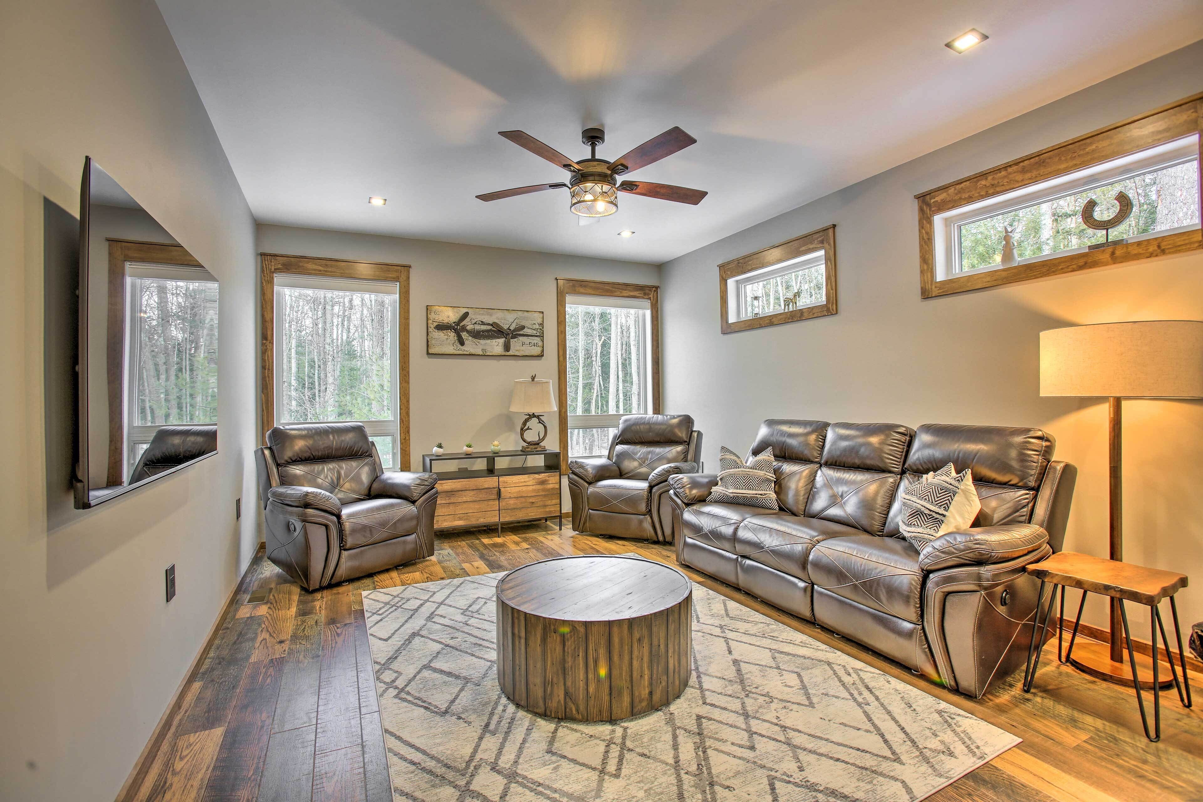 A spacious living room with leather sofas, a round coffee table, and large windows offering views of trees.