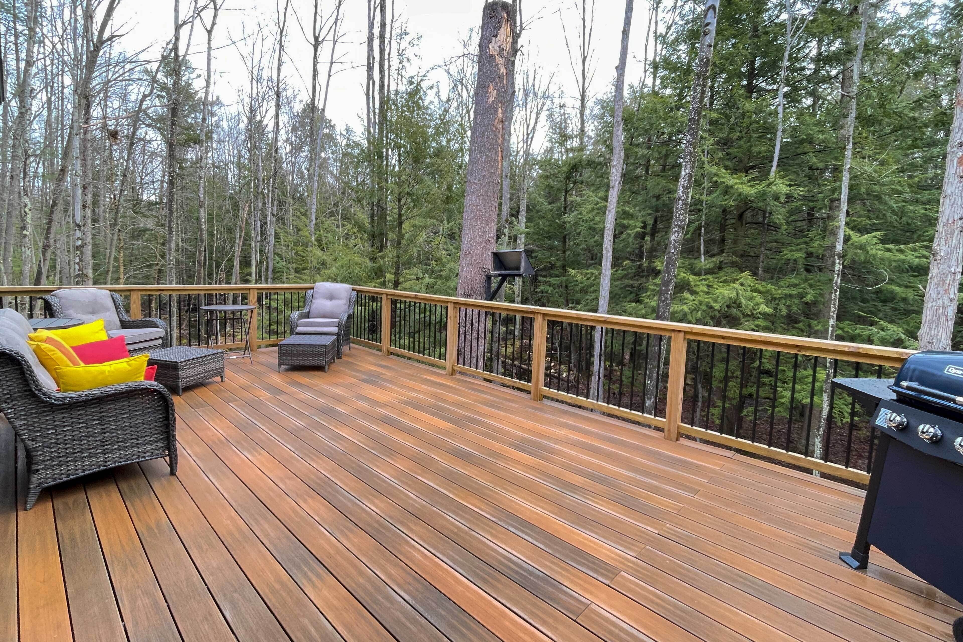 Un terrazzo in legno con mobili da esterno e una griglia, immerso in una foresta.