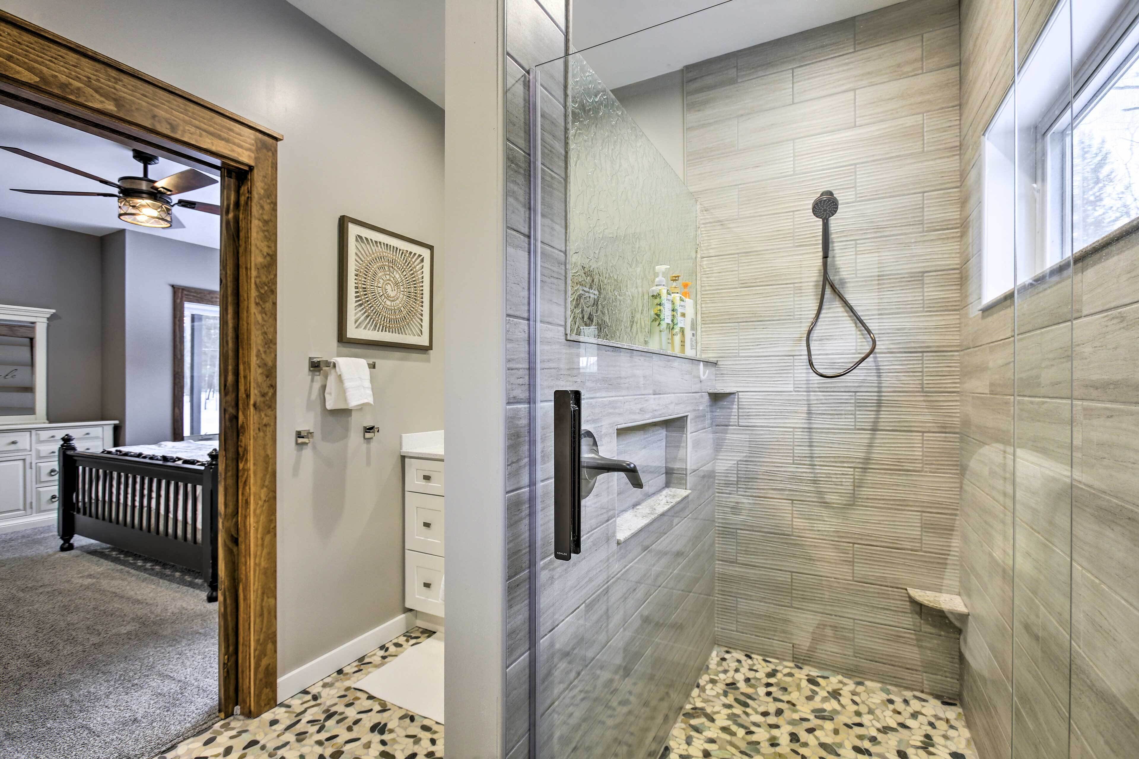 A modern bathroom with a glass shower enclosure, a wooden-framed door, and a patterned floor.