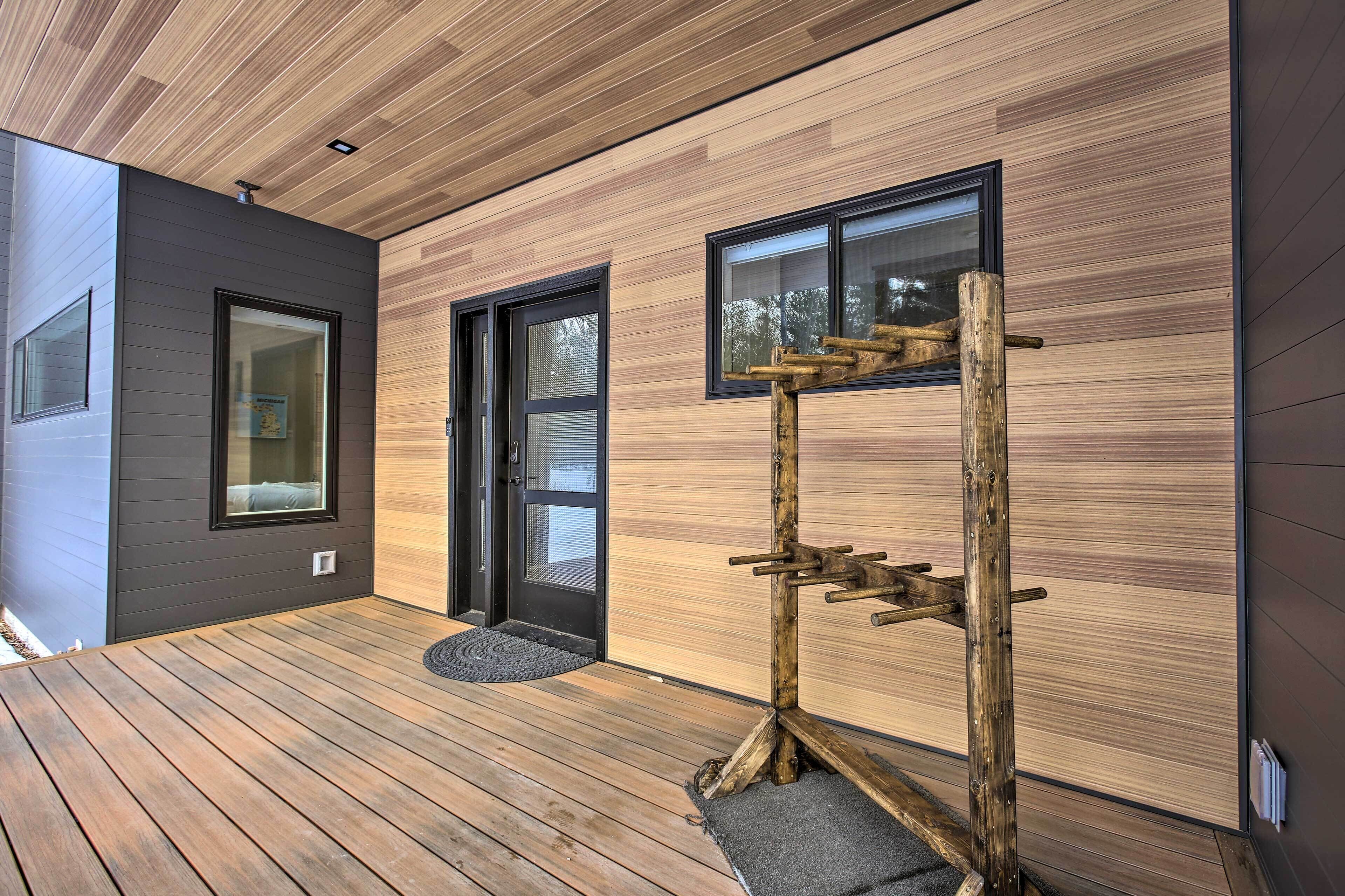 Exterior moderno con terraza de madera, puerta negra y ventana con estructura de madera.