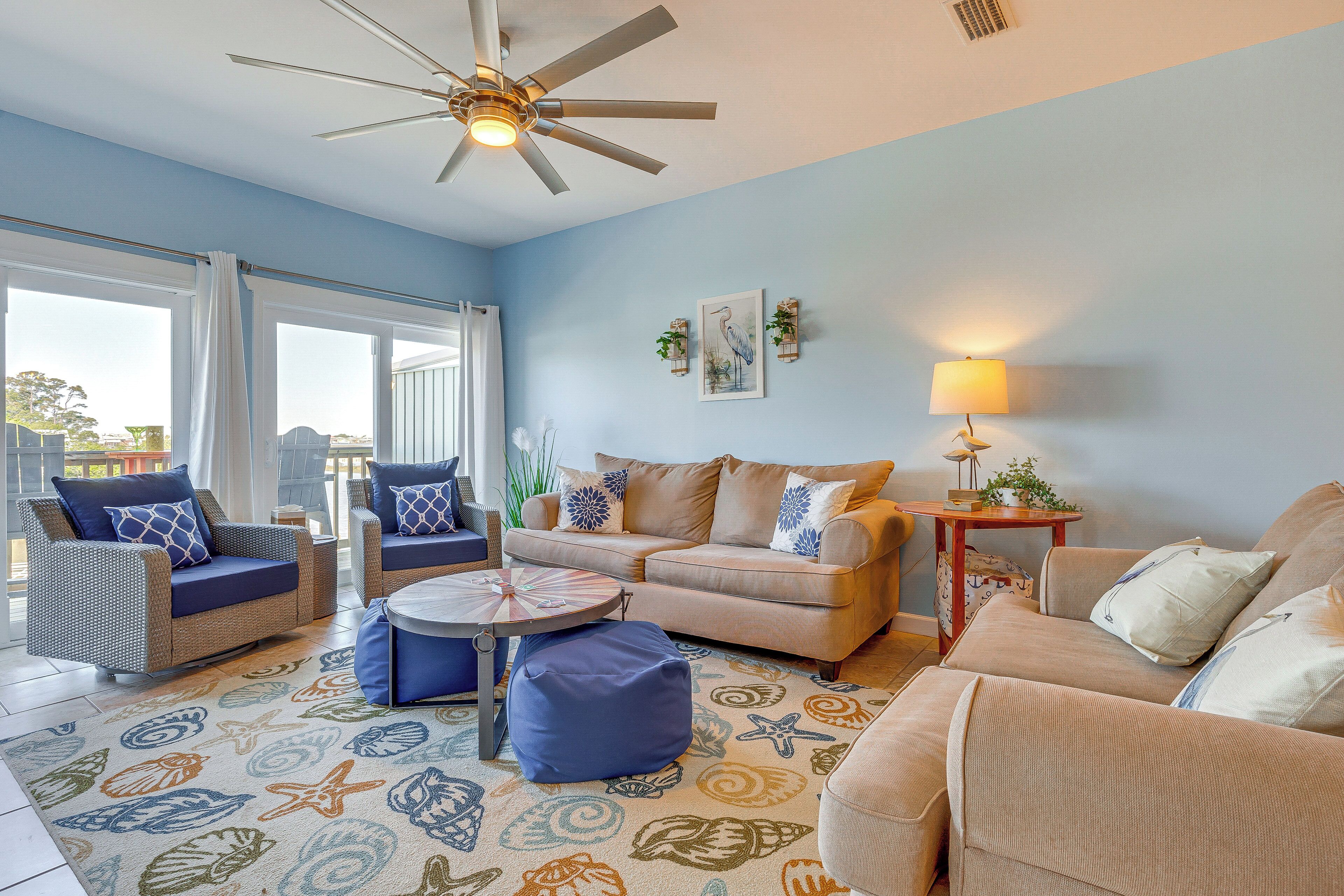Una sala de estar con ventilador de techo, un sofá color beige, un sillón azul y un tapete estampado.