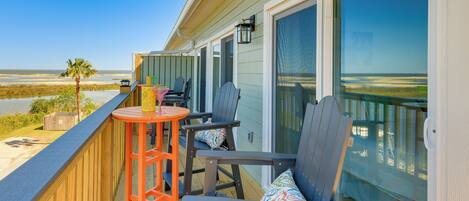 A balcony with two Adirondack chairs, a small orange table, and a view of the beach.