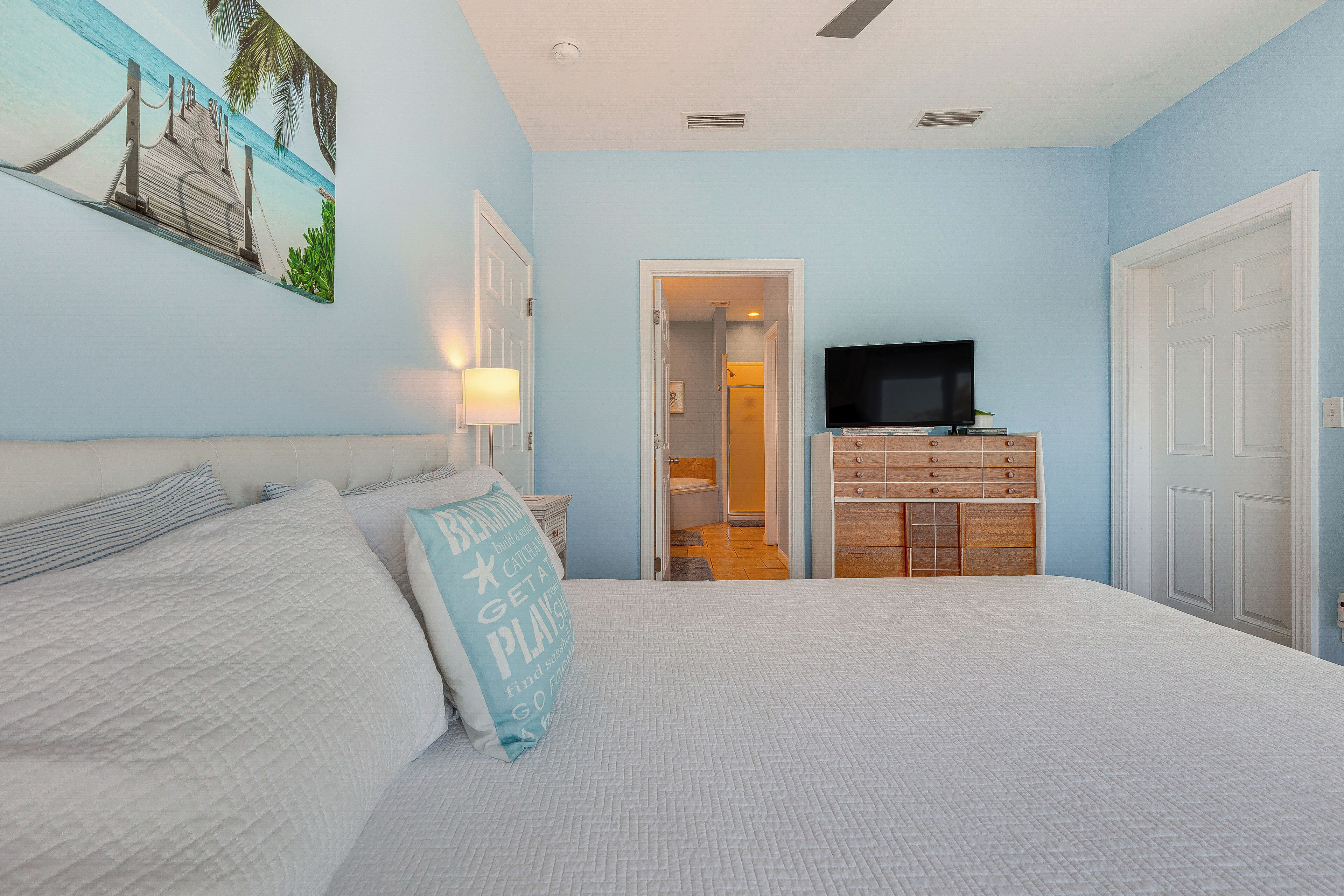 Une chambre à coucher comprenant un lit, une télévision, une commode et une porte donnant accès à une salle de bain.