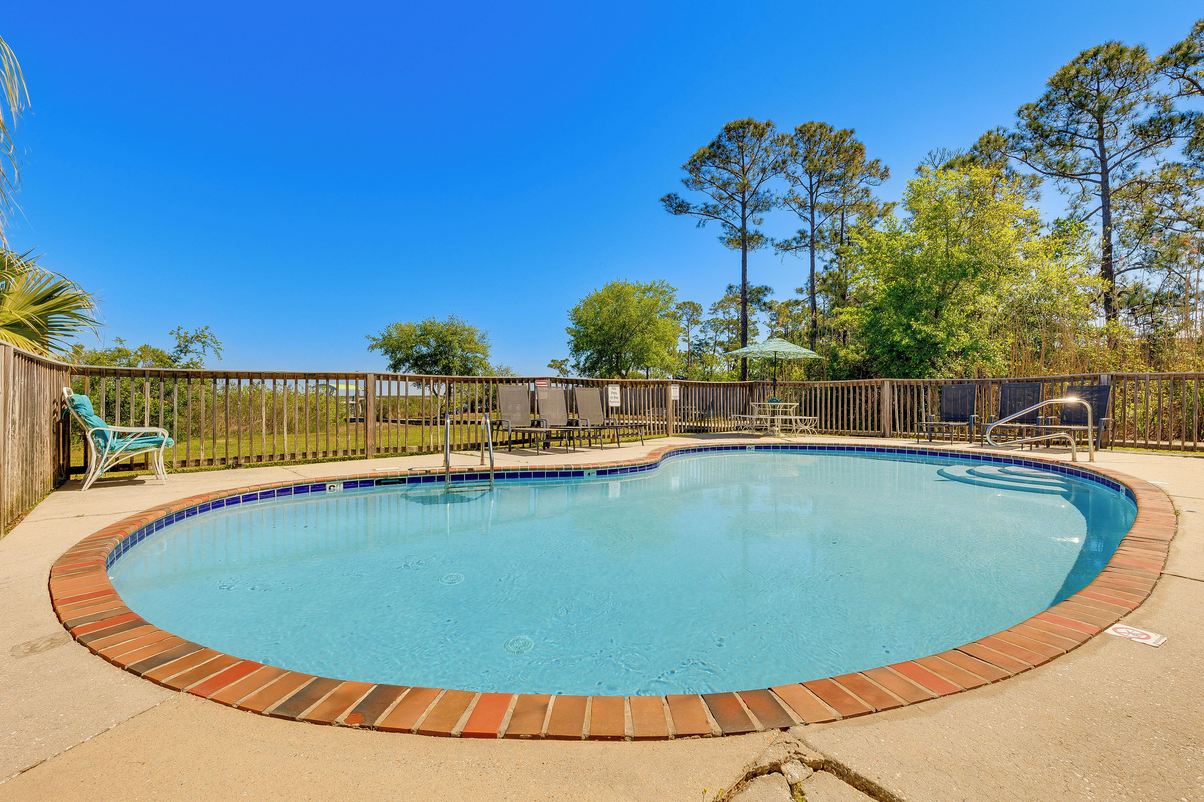 A circular pool with a brick border, surrounded by a wooden deck and a fence.