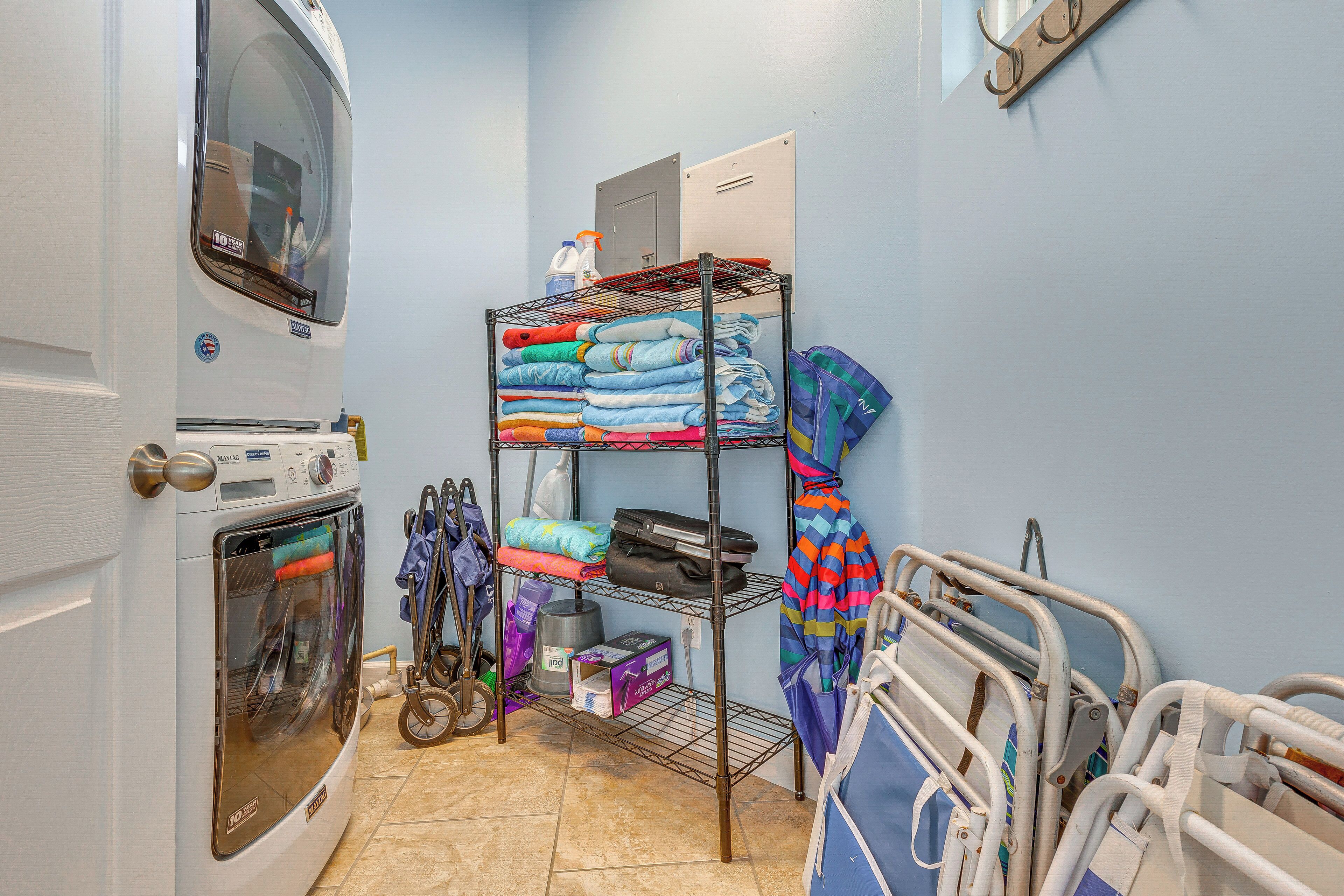 A laundry room with a washing machine, a drying rack, and a shelf with folded clothes.