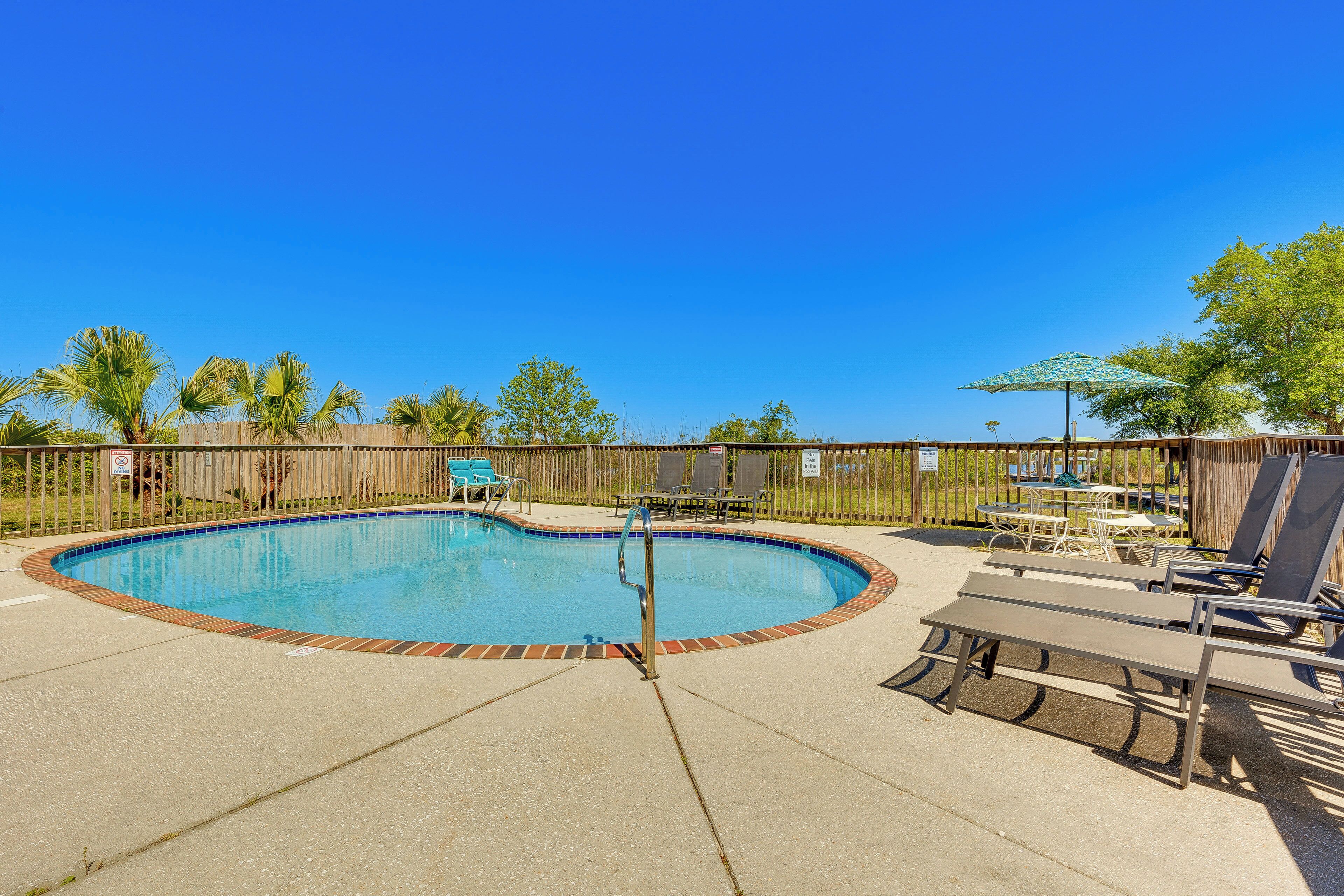 A swimming pool with a wooden fence, lounge chairs, and a picnic table.