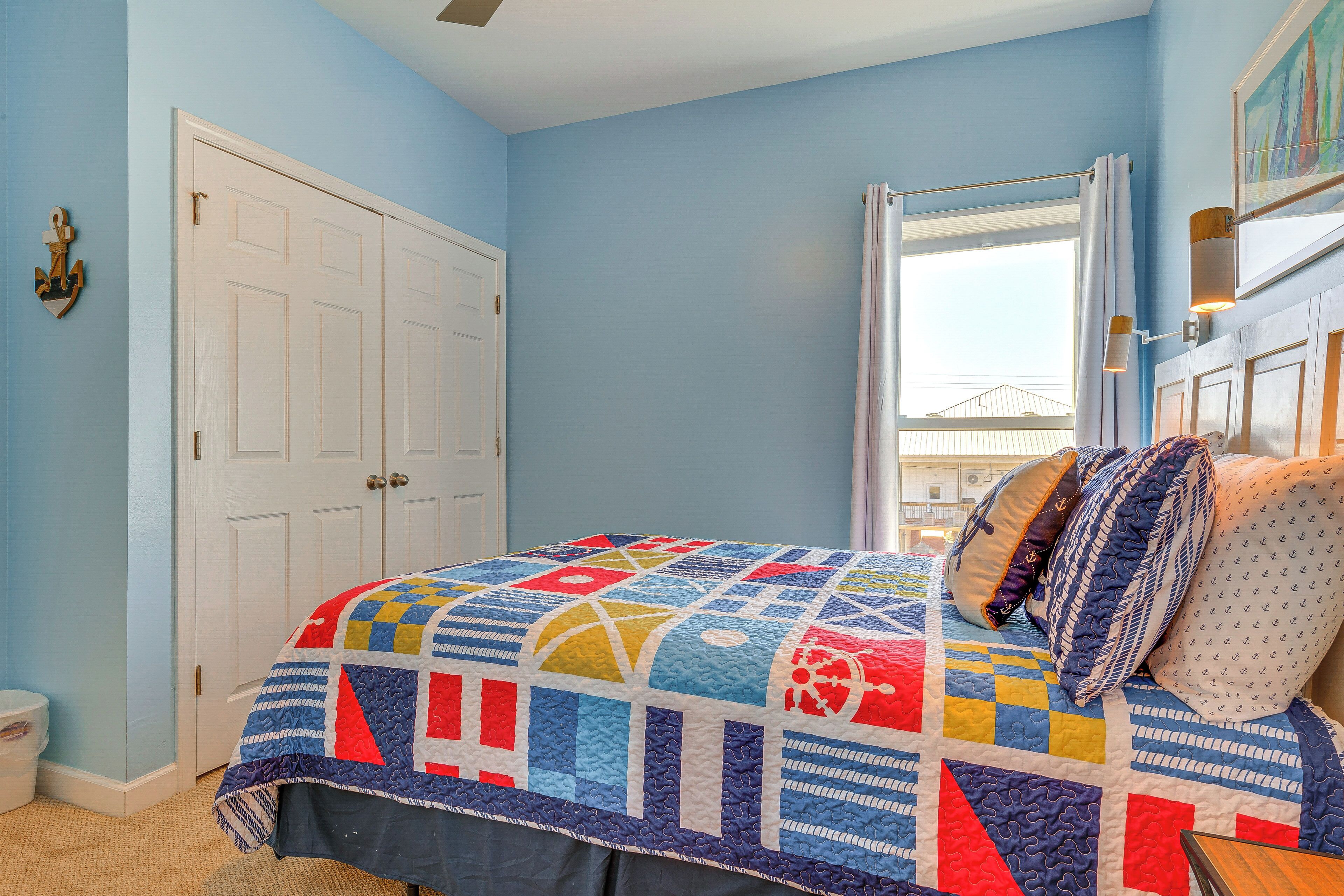 Une chambre à coucher avec un grand lit, une fenêtre avec des rideaux, une porte et un luminaire fixé au mur.