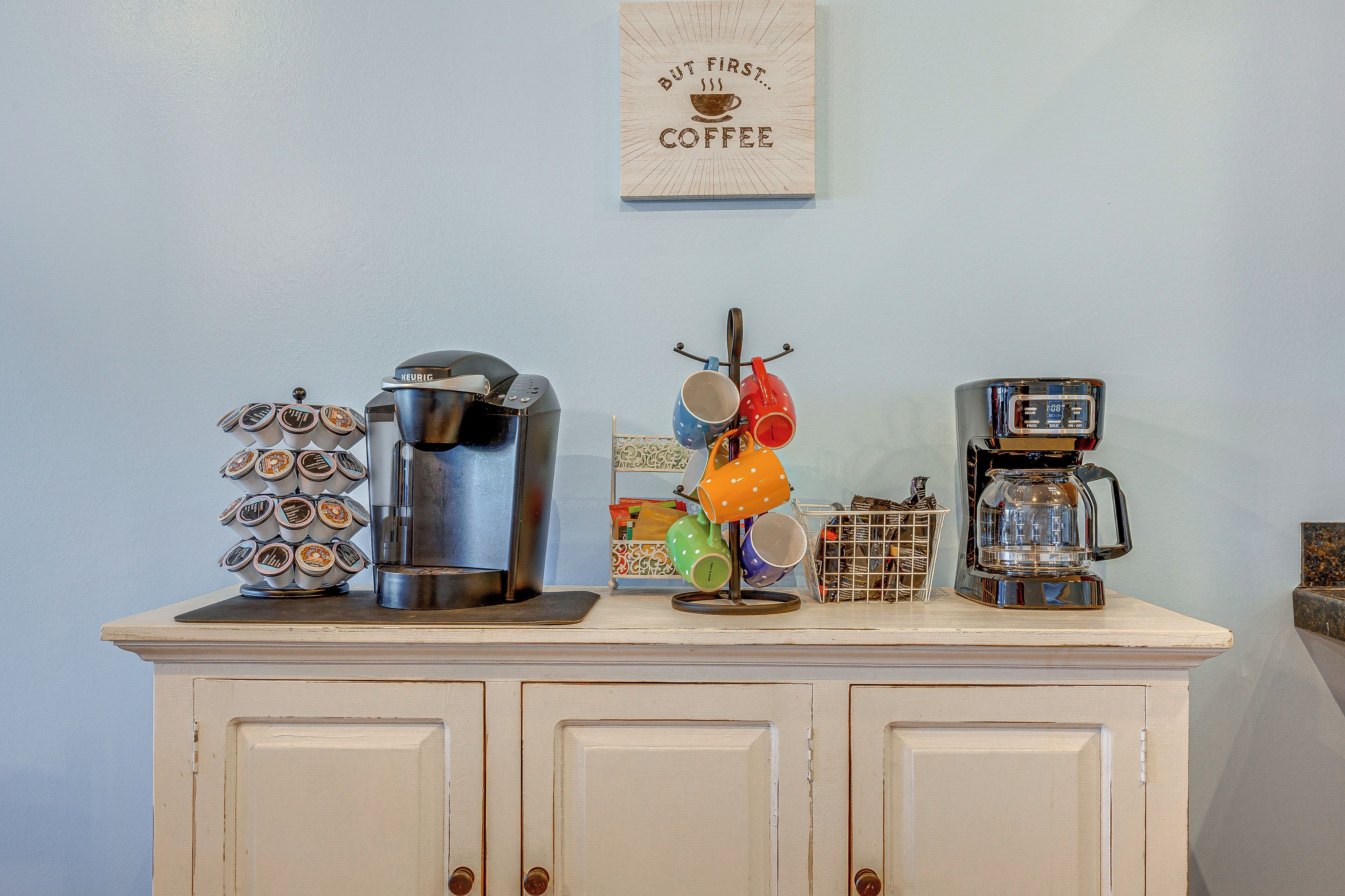 A kitchen counter with a coffee maker, a coffee pot, and a mug rack.