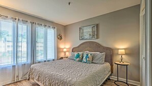 A bedroom with a large bed, two bedside lamps, a decorative headboard, and a view of the outdoors through sheer curtains. - Family-friendly Condo w/ Pools + Tennis Courts! (Hilton Head Island)