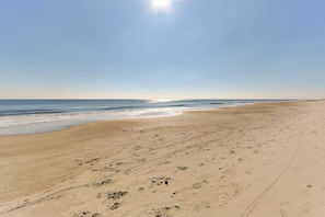 Een breed zandstrand met voetafdrukken en sporen van banden, dat uitloopt in de oceaan onder een heldere lucht.