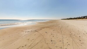 A wide sandy beach with footprints and tire tracks, leading to the ocean.