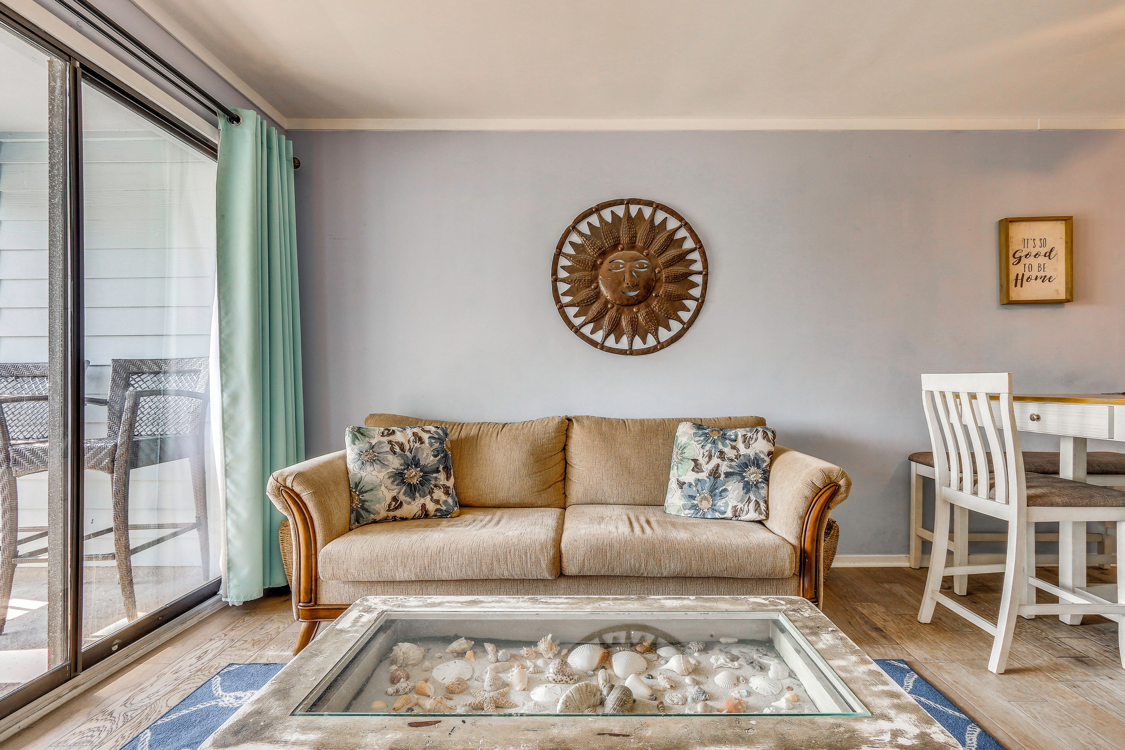 A living room with a sofa, a glass coffee table with seashells, a wall decoration, and a framed quote on the wall.