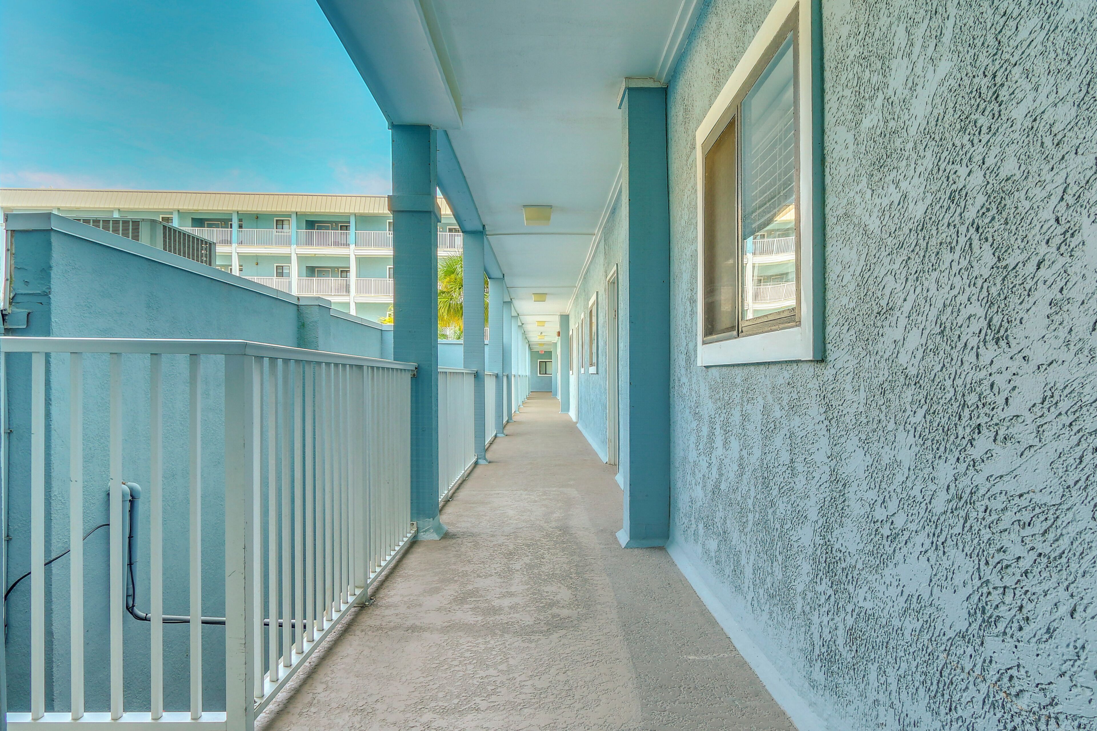 A corridor with a concrete floor, blue walls, and white railings.