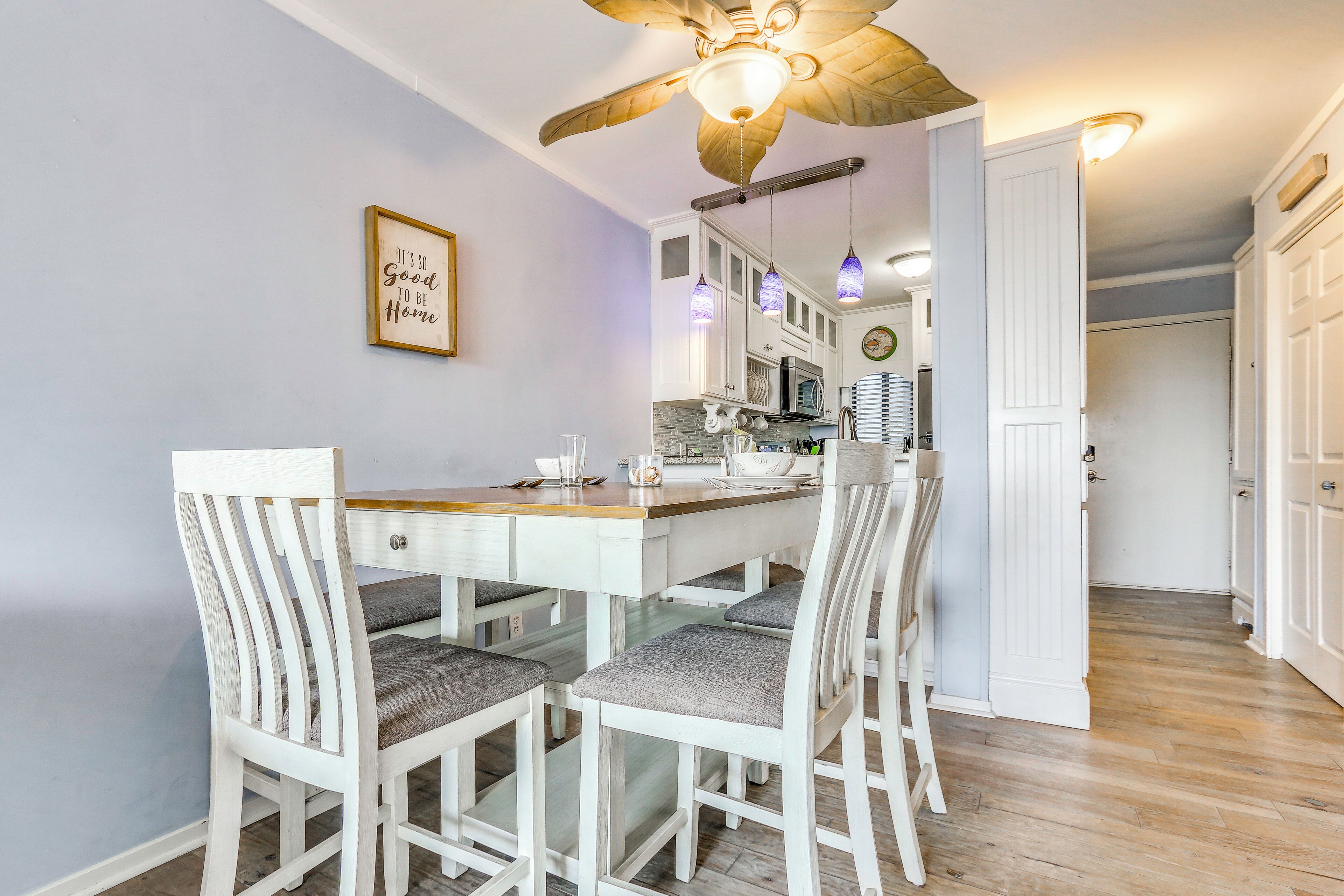 A dining area with a wooden table and chairs, a ceiling fan, and a kitchen in the background.