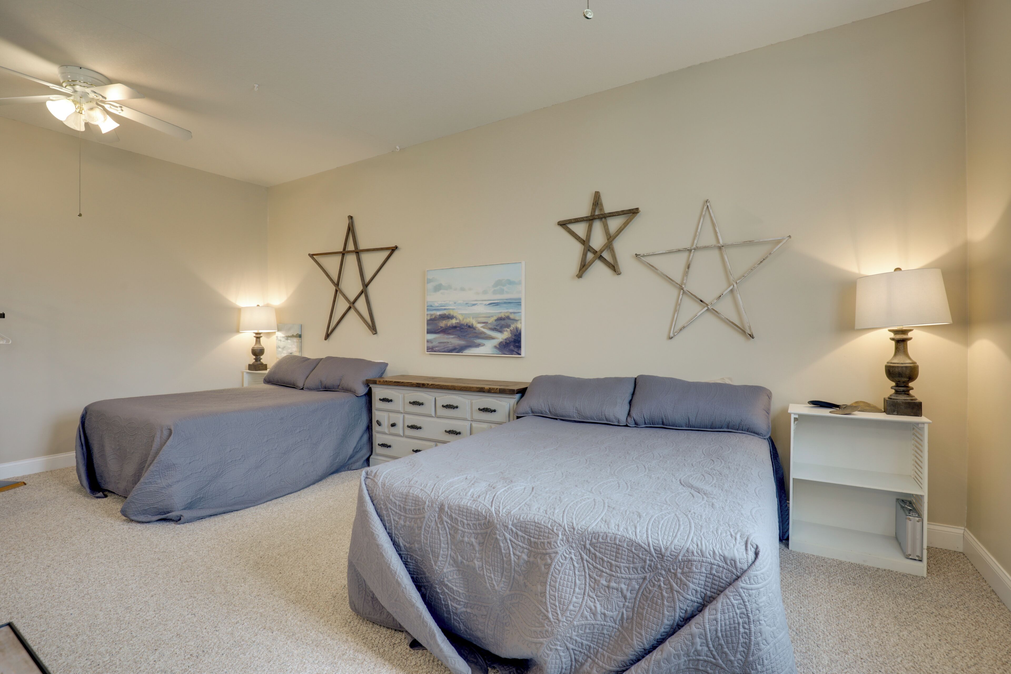 A bedroom with two beds, a ceiling fan, wall-mounted lamps, and a star decoration.
