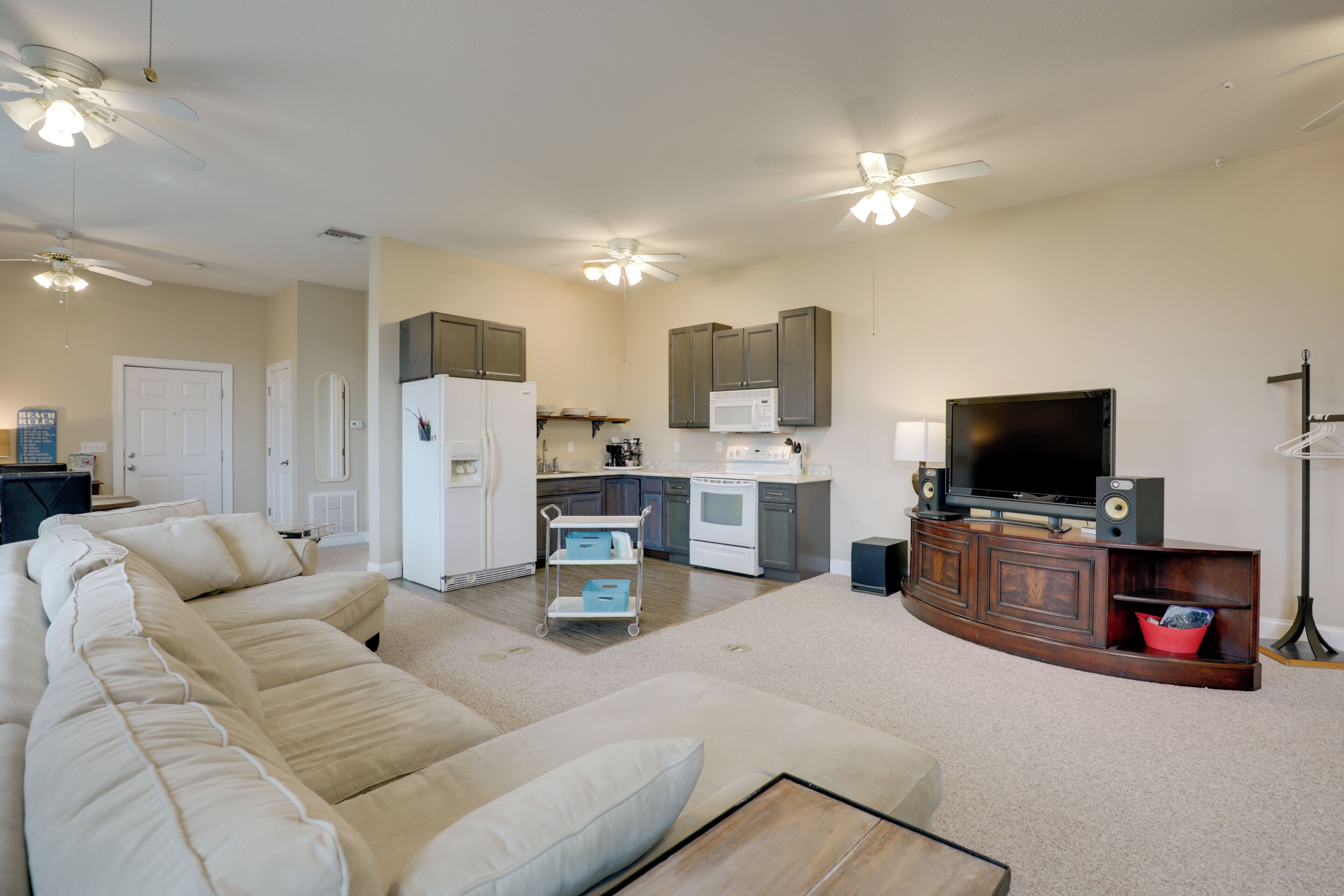 A modern living room with a sectional sofa, a flat-screen TV, and a kitchen area with cabinets and appliances.