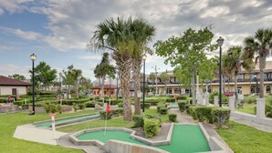 Un parcours de mini-golf doté d’un green en gazon, entouré de palmiers et d’une haie bien entretenue.