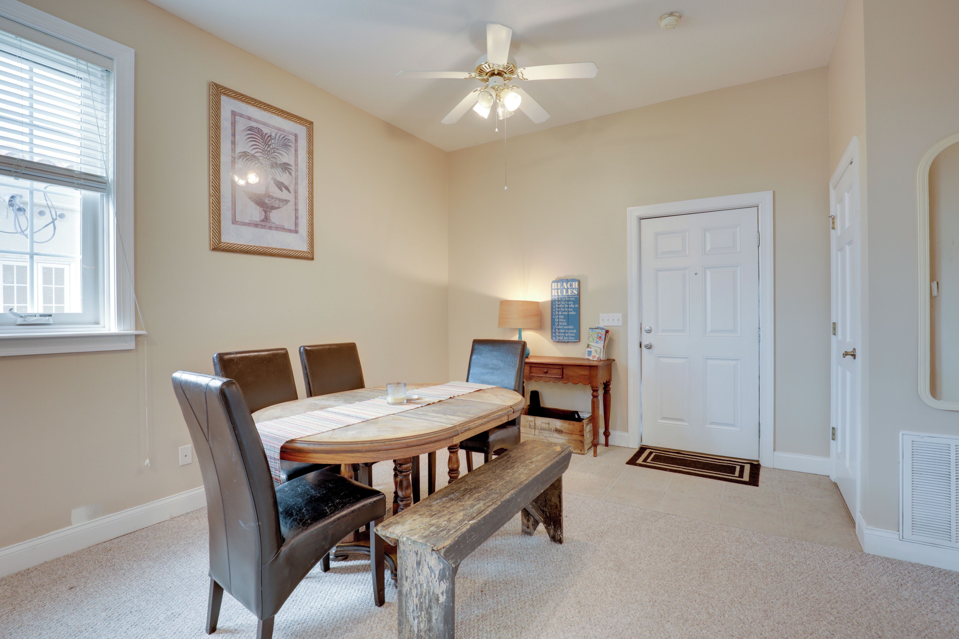 A dining area with a round table, chairs, a bench, a ceiling fan, a lamp, and a door.