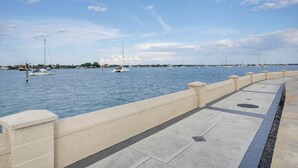 Une promenade en bord de mer, agrémentée d’une balustrade en pierre, où l’eau est calme et où l’on peut admirer plusieurs bateaux.