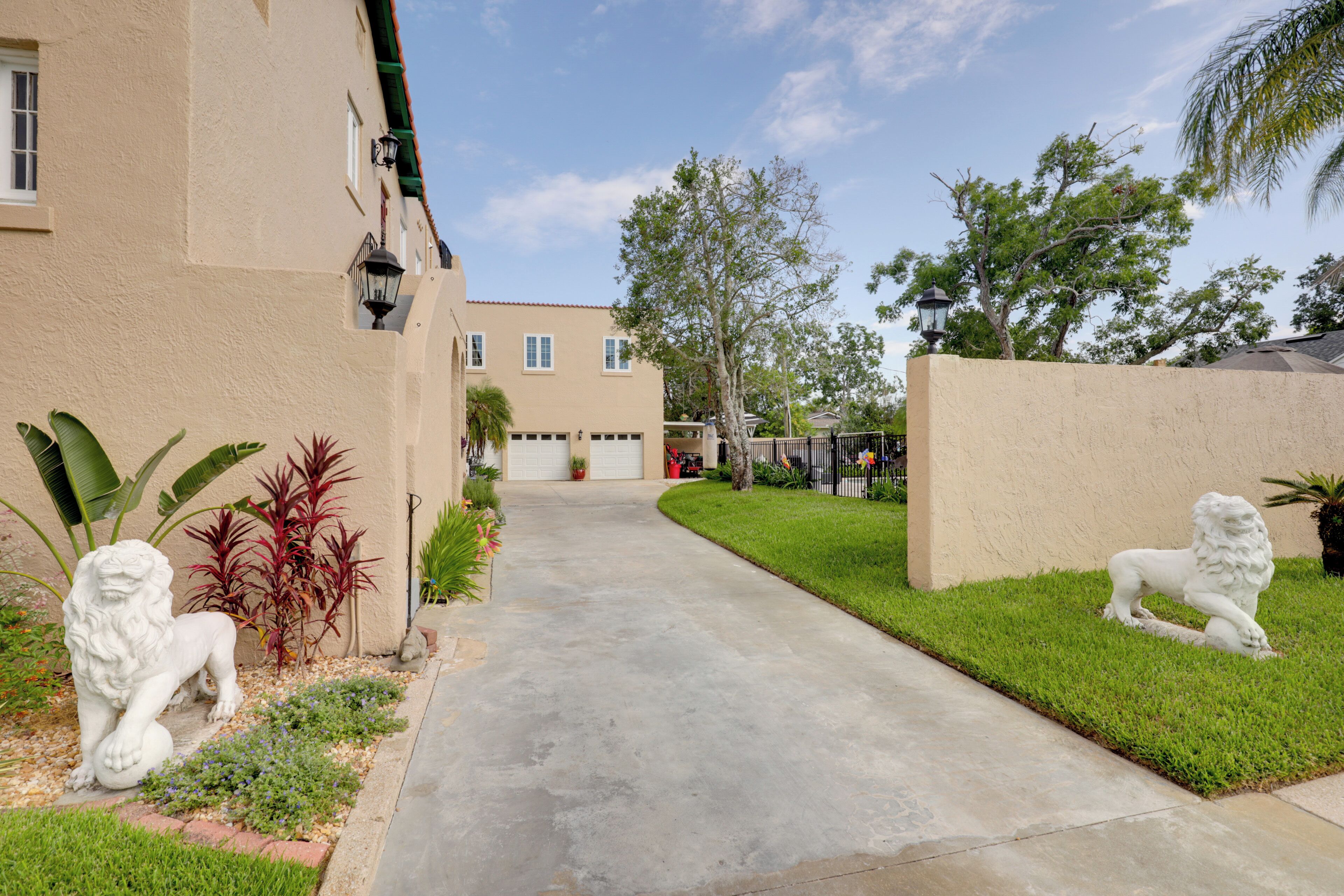 A residential driveway with a concrete path, two white lion statues, and a well-maintained lawn.