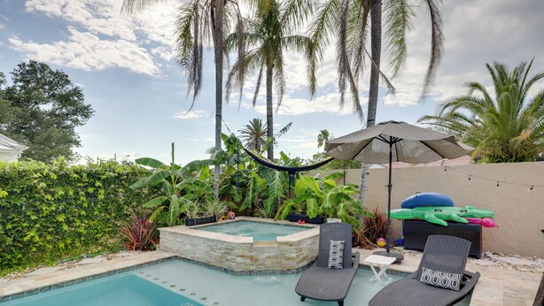 Une piscine dotée de chaises longues et d’un jacuzzi, le tout entouré de palmiers et de verdure.