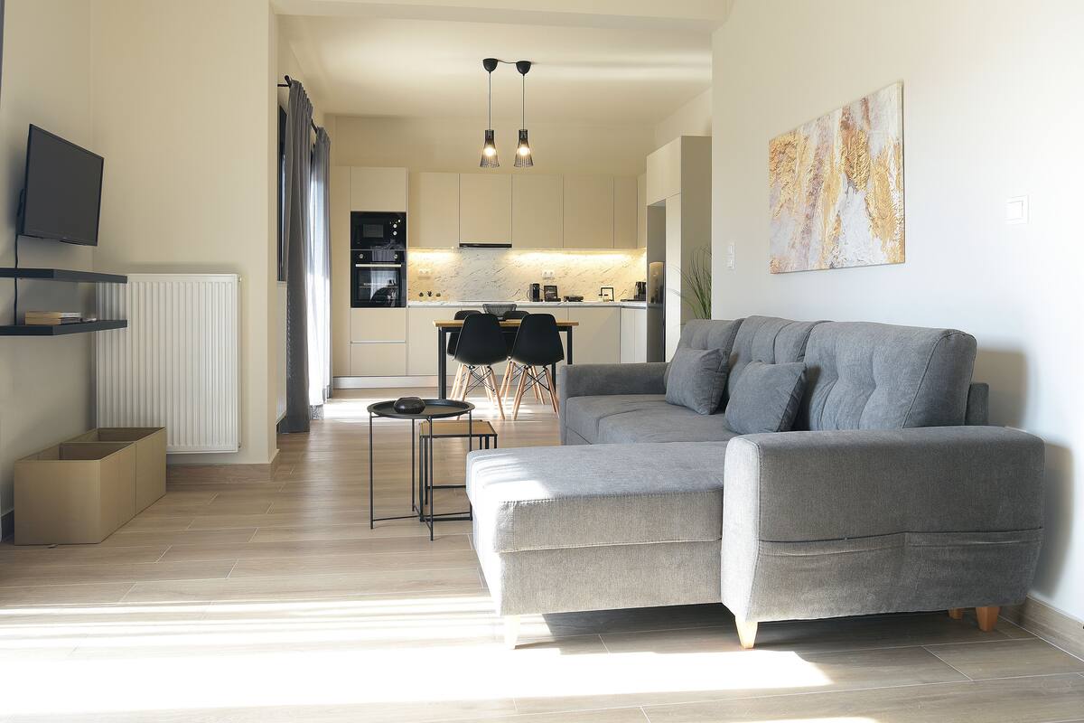 A modern living room with a grey sofa, a coffee table, and a TV on a shelf.