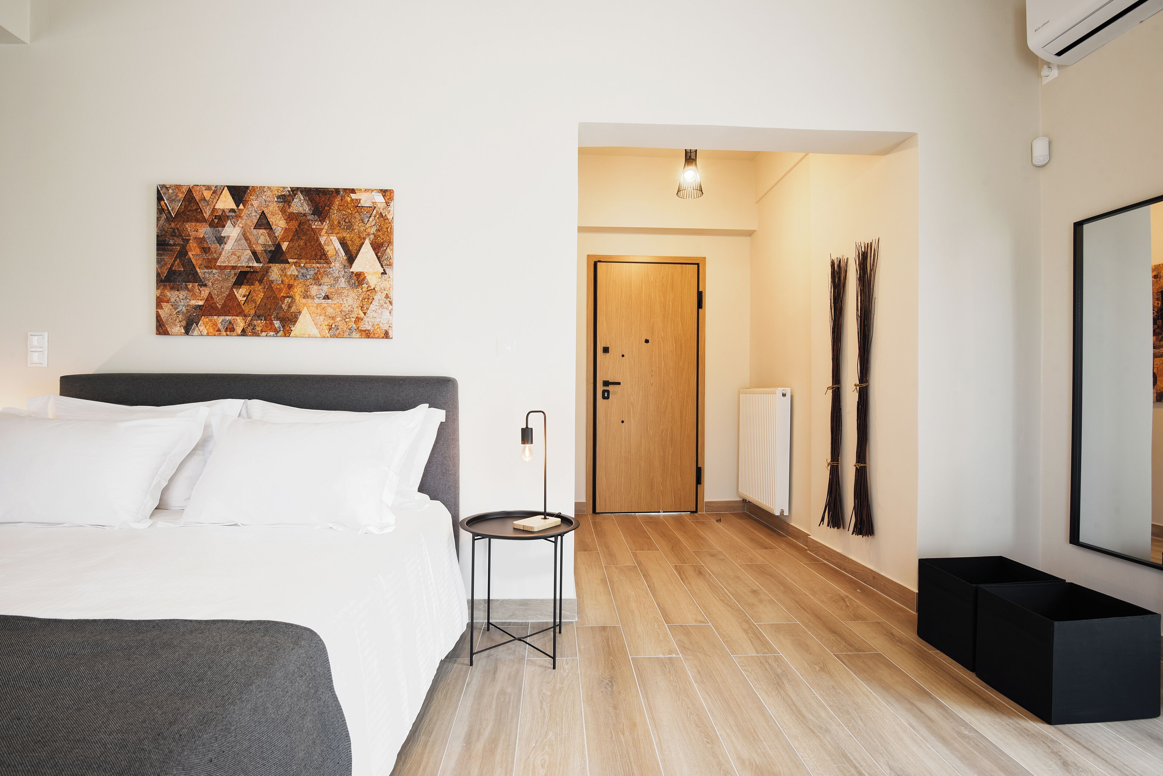 Habitación de hotel moderna con cama, una mesita, puerta de madera y una obra de arte colgada en la pared.